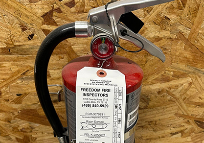 Firefighter inspecting a fire extinguisher, representing Freedom Fire Inspectors' service.